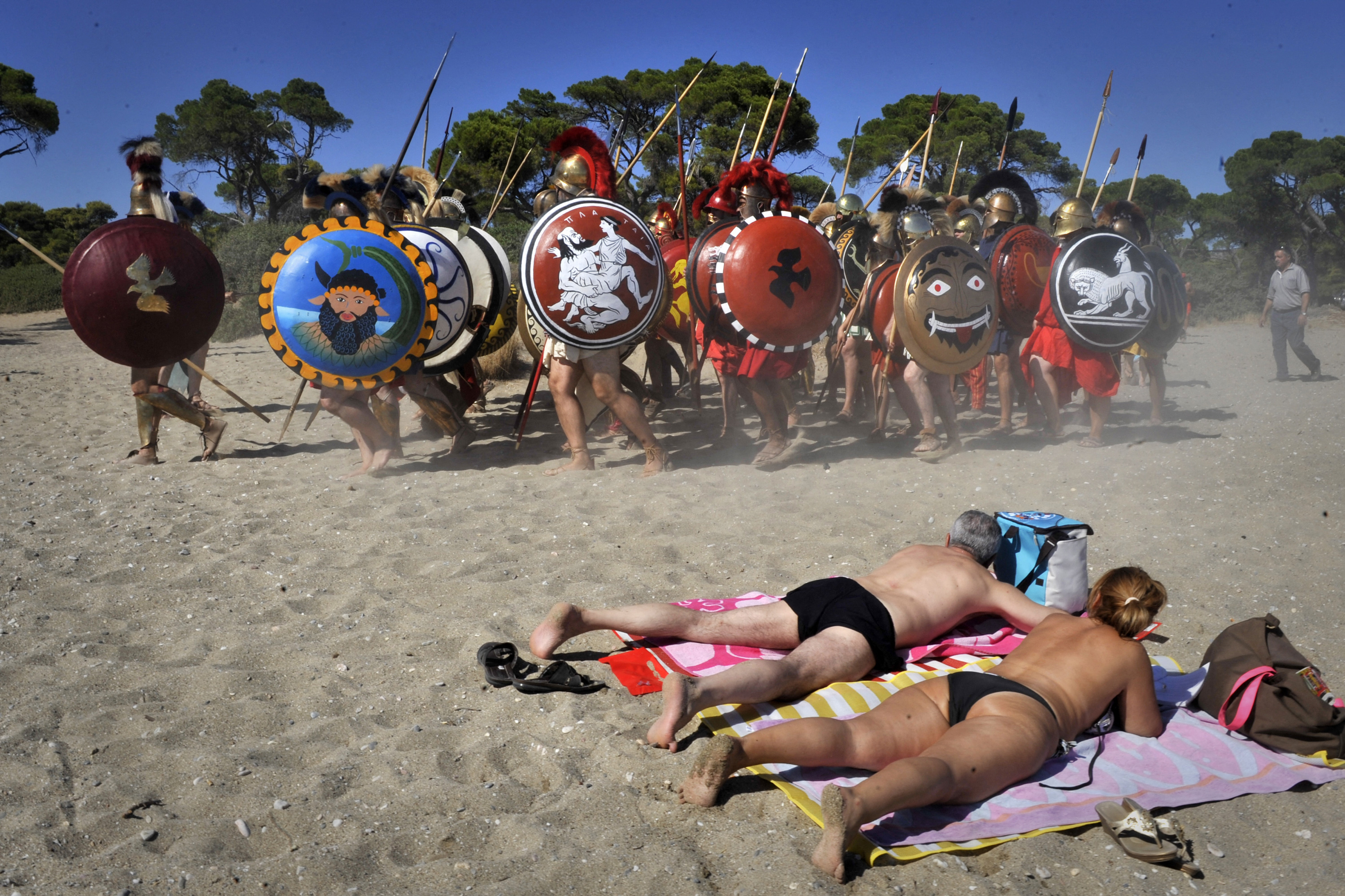 People dressed as Greek citizen-soldiers march toward a reenactment of the 490 B.C. Battle of Marathon, where the fate of Europe dramatically changed over 2,500 years ago. 
© Louisa Gouliamaki/AFP/Getty
TOPSHOT - TO GO WITH AFP STORY: History brought to life in Battle of Marathon re-enactment
Sunbathers watch Italian re-enactors dressed as Greek hoplites march to perform the 490 B.C battle of Marathon at the Marathon Bay on September 10, 2011. Sweating beneath heavy armour, a group of die-hard archaeology fans brought the Battle of Marathon to life this weekend near the field where the fate of Europe dramatically changed 2,500 years ago. Gathering from Europe, North America and Australia, the re-enacters staged a three-day event of combat, archaic culture revival and commemoration at Marathon Bay never before seen in Greece despite its rich archaeological heritage. AFP PHOTO / LOUISA GOULIAMAKI (Photo by LOUISA GOULIAMAKI / AFP) (Photo by LOUISA GOULIAMAKI/AFP via Getty Images)